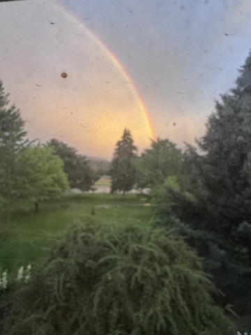 After the Rain - A rainbow over wooded landscape viewed through rain-specked window