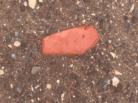A single red brick fragment resting on dry earth and gravel, Loreto, January 2026