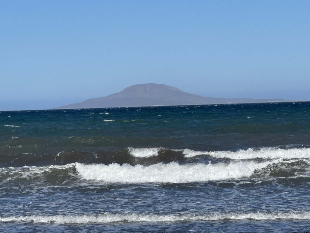 Waves breaking on the Sea of Cortez with a volcanic island in the distance under a pale sky