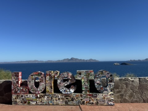 The Loreto letter sign covered in stickers with the blue Sea of Cortez and mountains behind it