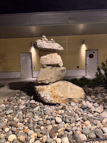 A stone cairn balanced carefully in the night outside a lit building, stones stacked in quiet equilibrium.
