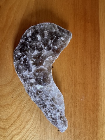 A dark crystalline rock fragment resting on a wooden surface, its fractured edges catching the light.